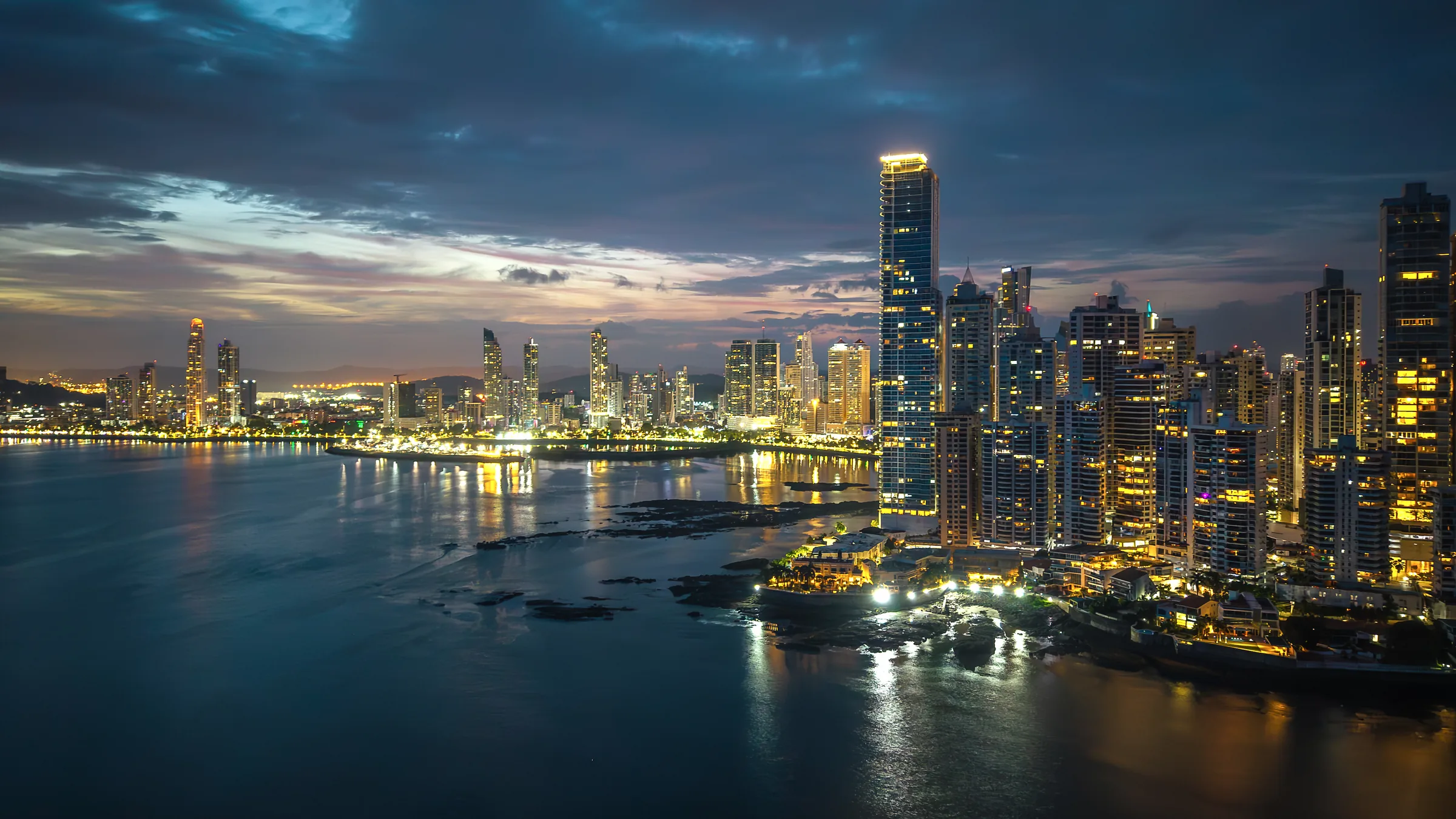 Rascacielos iluminados de Ciudad de Panamá junto a la bahía al anochecer.