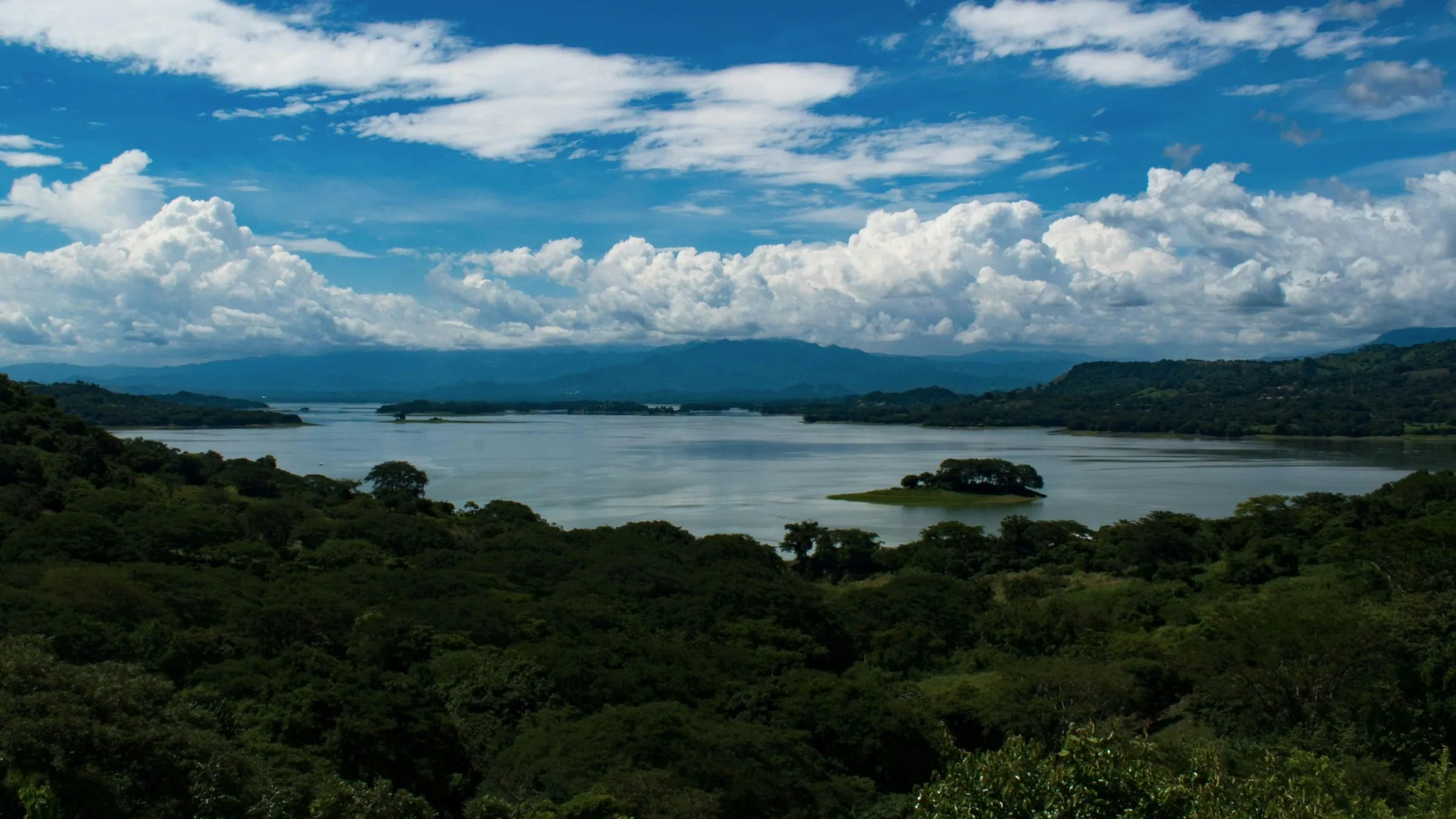 Lago con pequeñas islas y colinas, visto por encima de la vegetación.