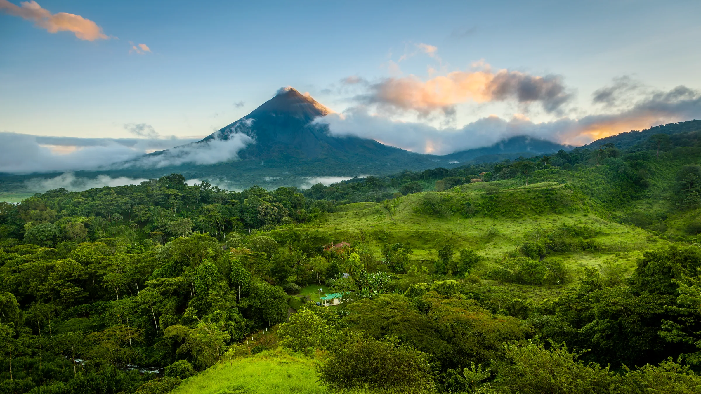 Volcán Arenal entre nubes sobre colinas cubiertas de bosque.